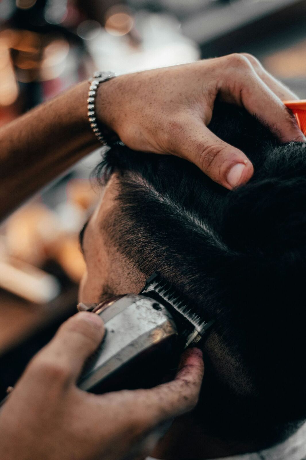 A barber's hands use electric clippers to trim the hair of a male client.