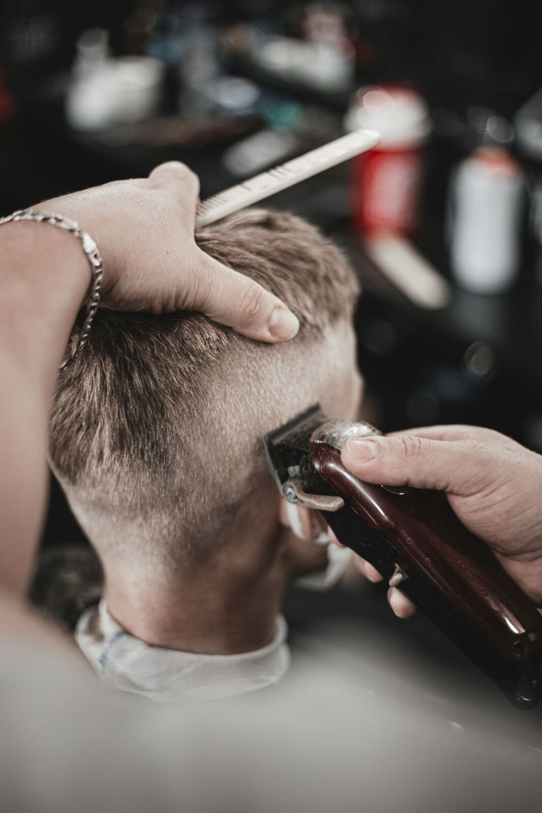 A barber uses clippers and a comb to cut the hair of a seated client.