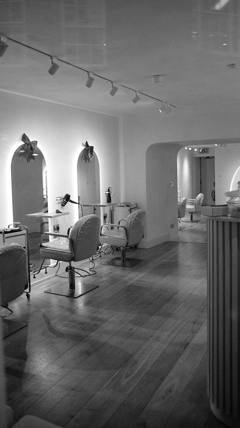 A black and white photo of an empty hair salon interior with styling chairs, mirrors, and a wooden floor.